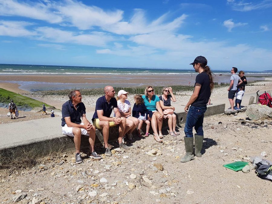 Gruppe hört Guide Jonas am Strand von Villers-sur-Mer zu.